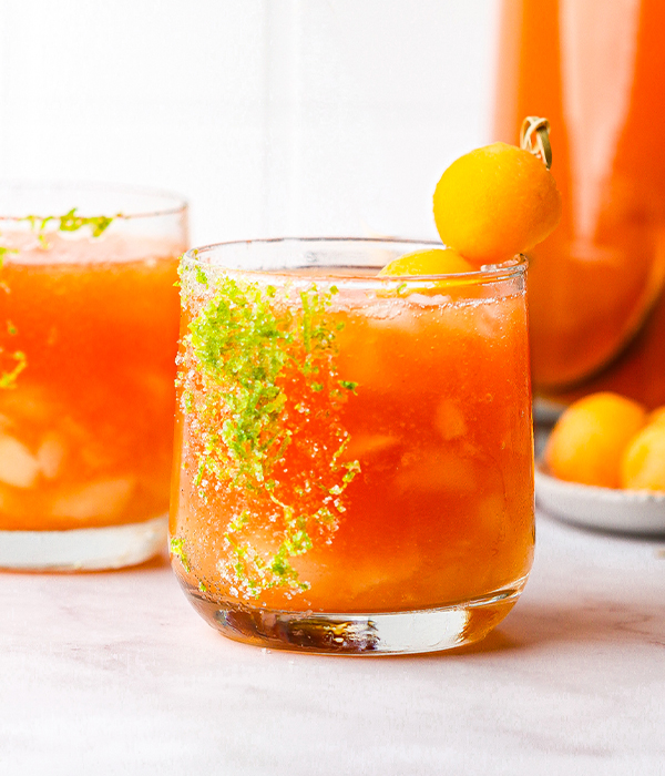 an orange drink garnished with a small fruit and lime zest